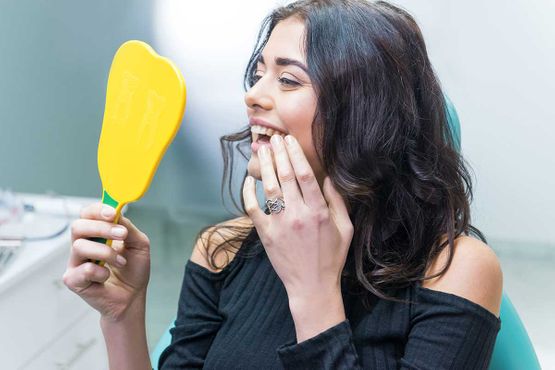 Frau mit dunklen Haaren erfreut sich an ihren Zähnen in einem gelben Spiegel